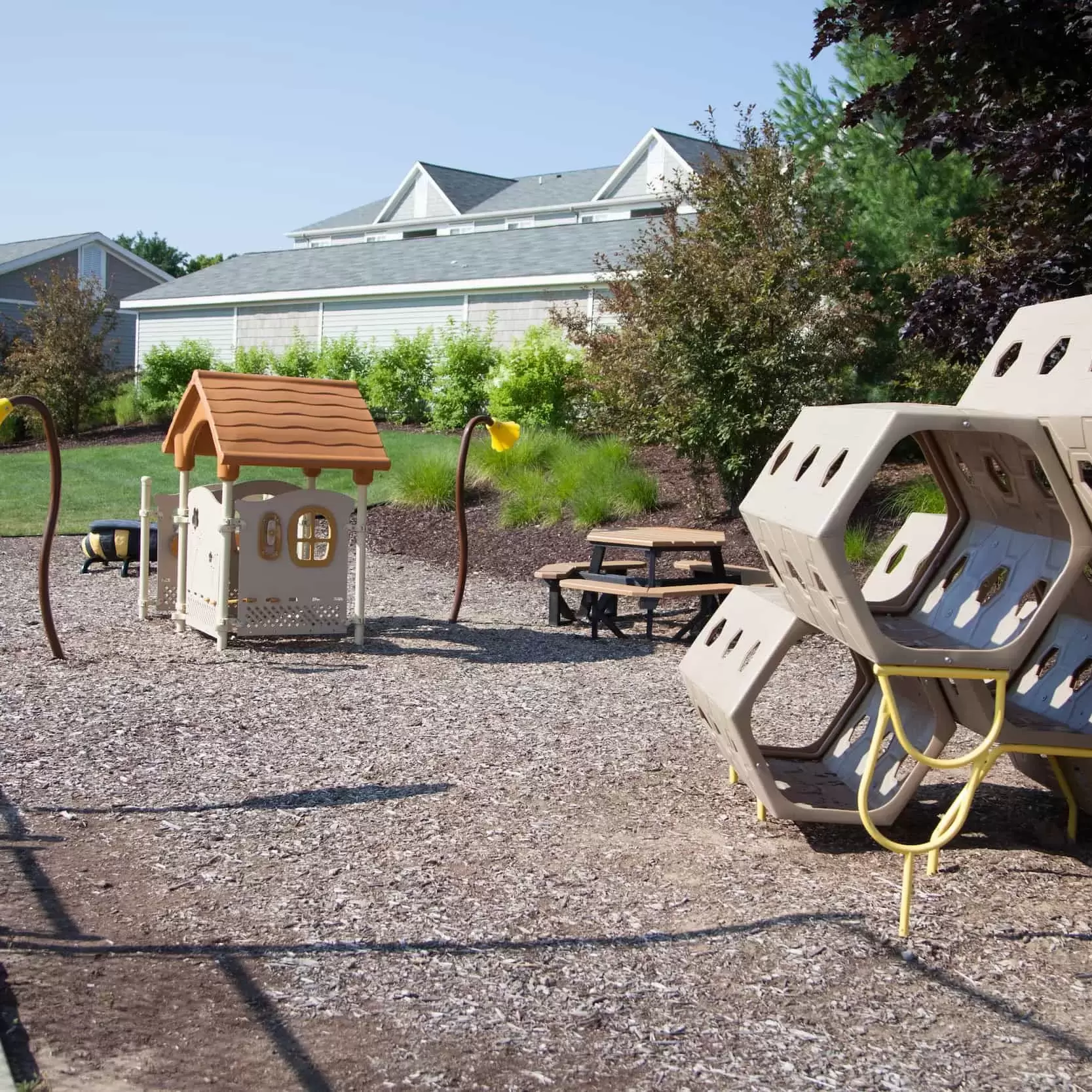 An outdoor play area for children has a picnic table, a play house, and a climbing structure.