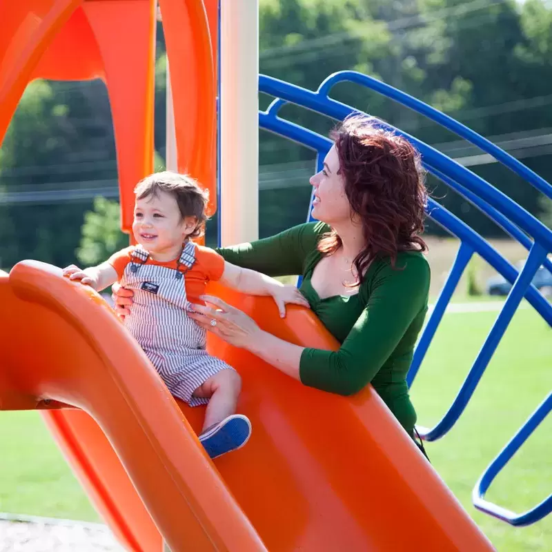 A young child and his mother are playing on the slide at the Tot Lot.