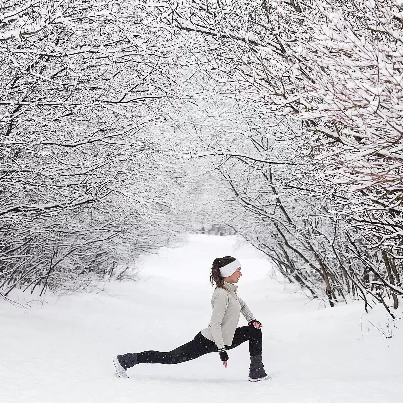 A woman doing a lunge in the middle of a snow-covered forest