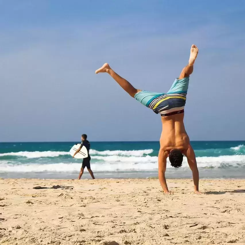 A man doing a cartwheel in front of the water on a beach.